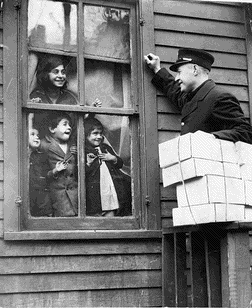 Excited chidren look out their window to see a Detroit policeman loaded with Christmas gifts. 