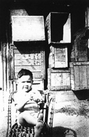 Peter Pratt in front of empty packing cases at the back of Wing Hing Long, about 1950.