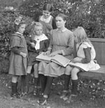 Photograph of a woman sitting on a park bench teaching four young girls Braille.